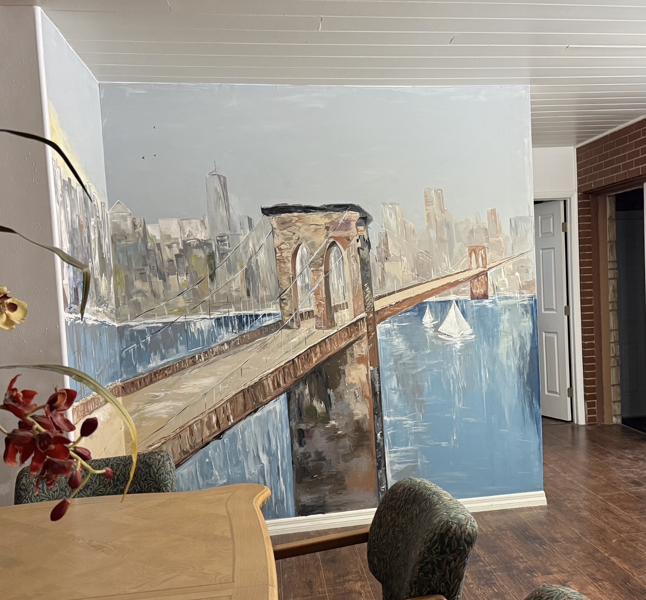 A hand-painted Brooklyn Bridge mural with city skyline and blue water in an interior room.